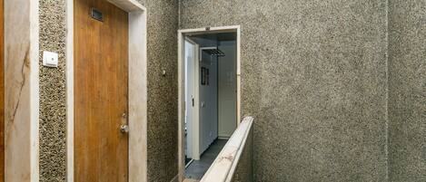A narrow hallway with textured walls, a wooden door, and a white railing.