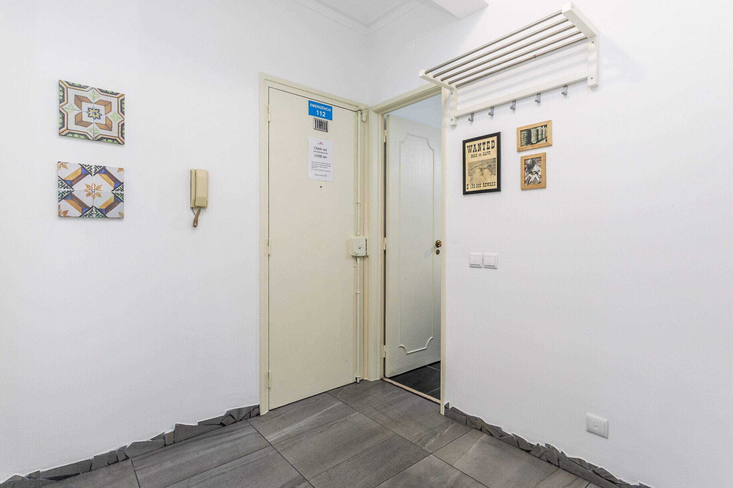 Un pasillo con una puerta marcada con el número 112, una luz empotrada en la pared y una rejilla de ventilación.
