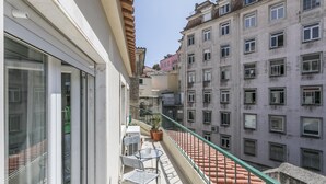 Un balcon avec une table et des chaises, un pot de fleurs et un escalier à revêtement de tuiles rouges.