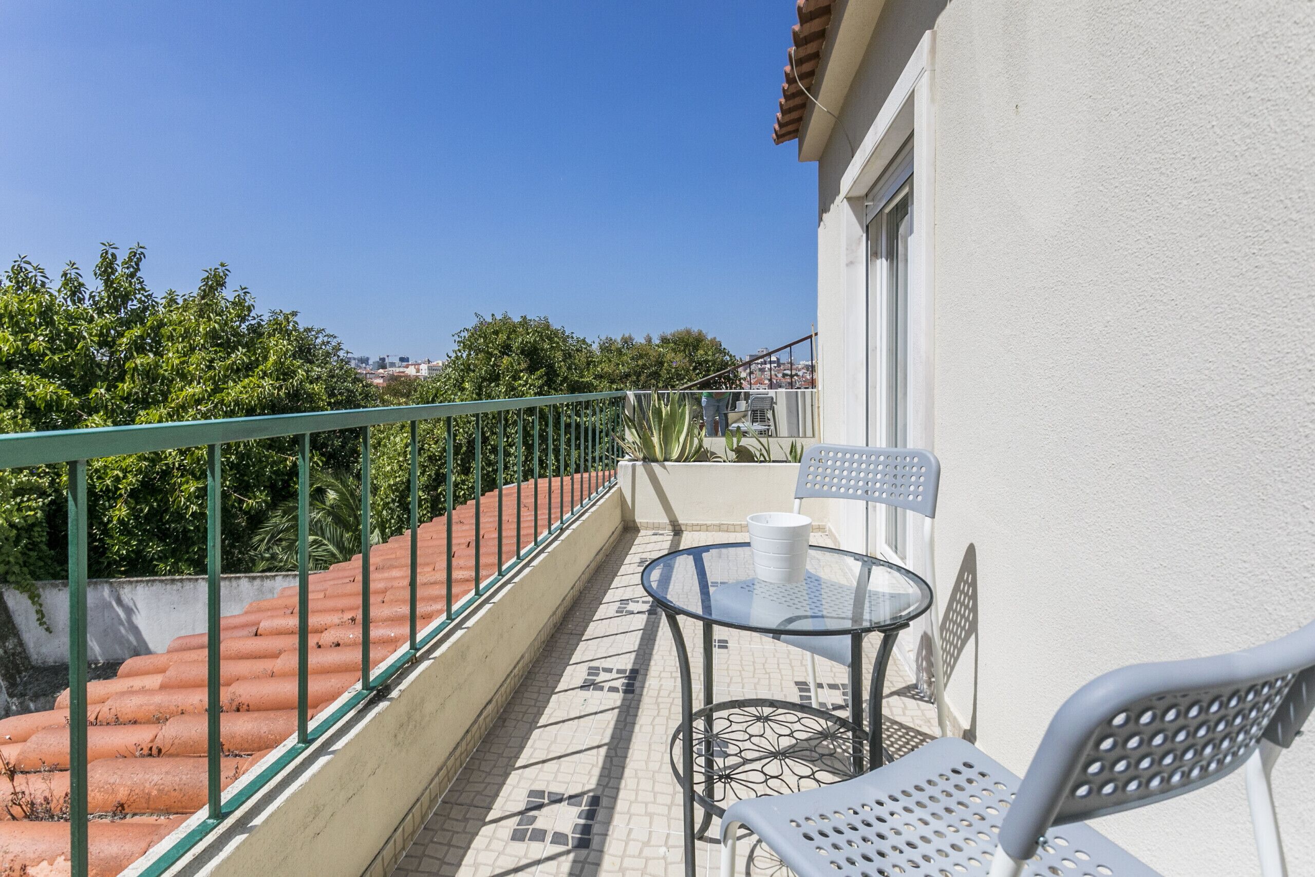 Un balcon avec une balustrade en métal, une petite table avec des chaises et un pot de fleurs.
