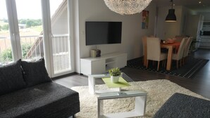 Ein modernes Wohnzimmer mit Flachbildfernseher, Glastisch und einer Couch.