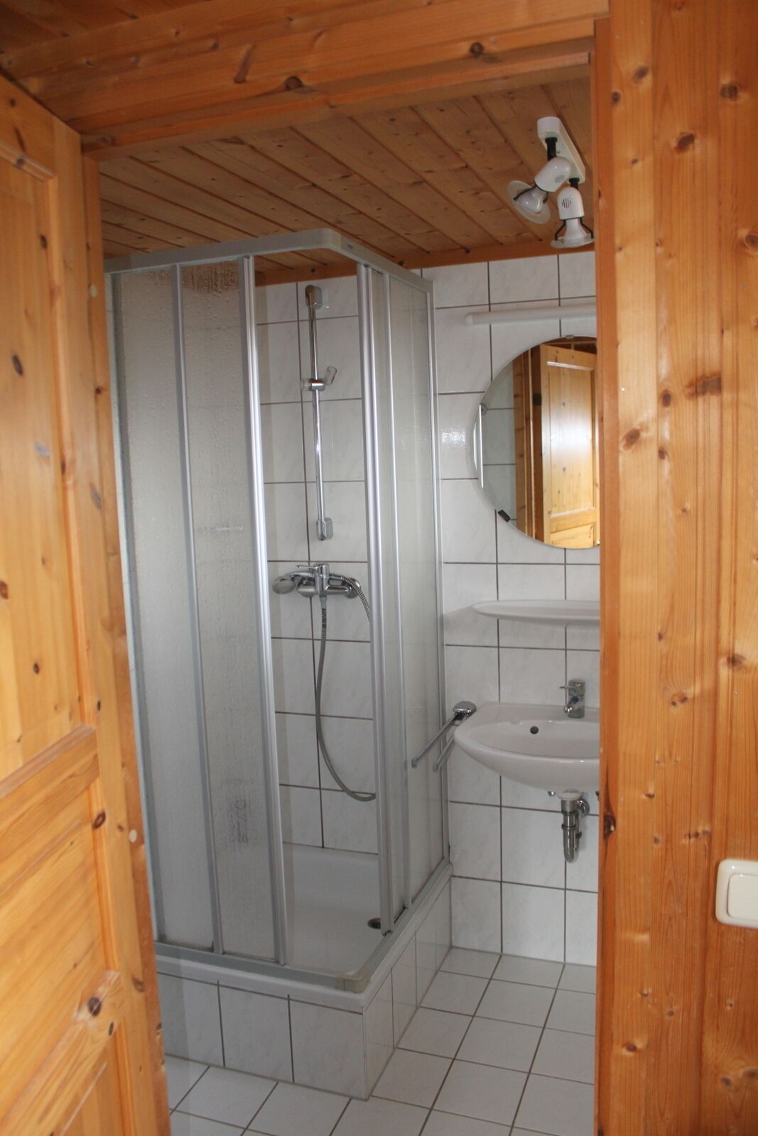 Une salle de bain aux murs lambrissés, dotée d’une douche à parois de verre, d’un lavabo et d’un miroir.