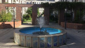 A circular fountain with water jets in the center, surrounded by a tiled border with mosaic patterns.