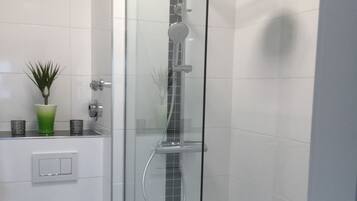 A modern bathroom with a glass-enclosed shower, a toilet, and a small green plant on the sink.