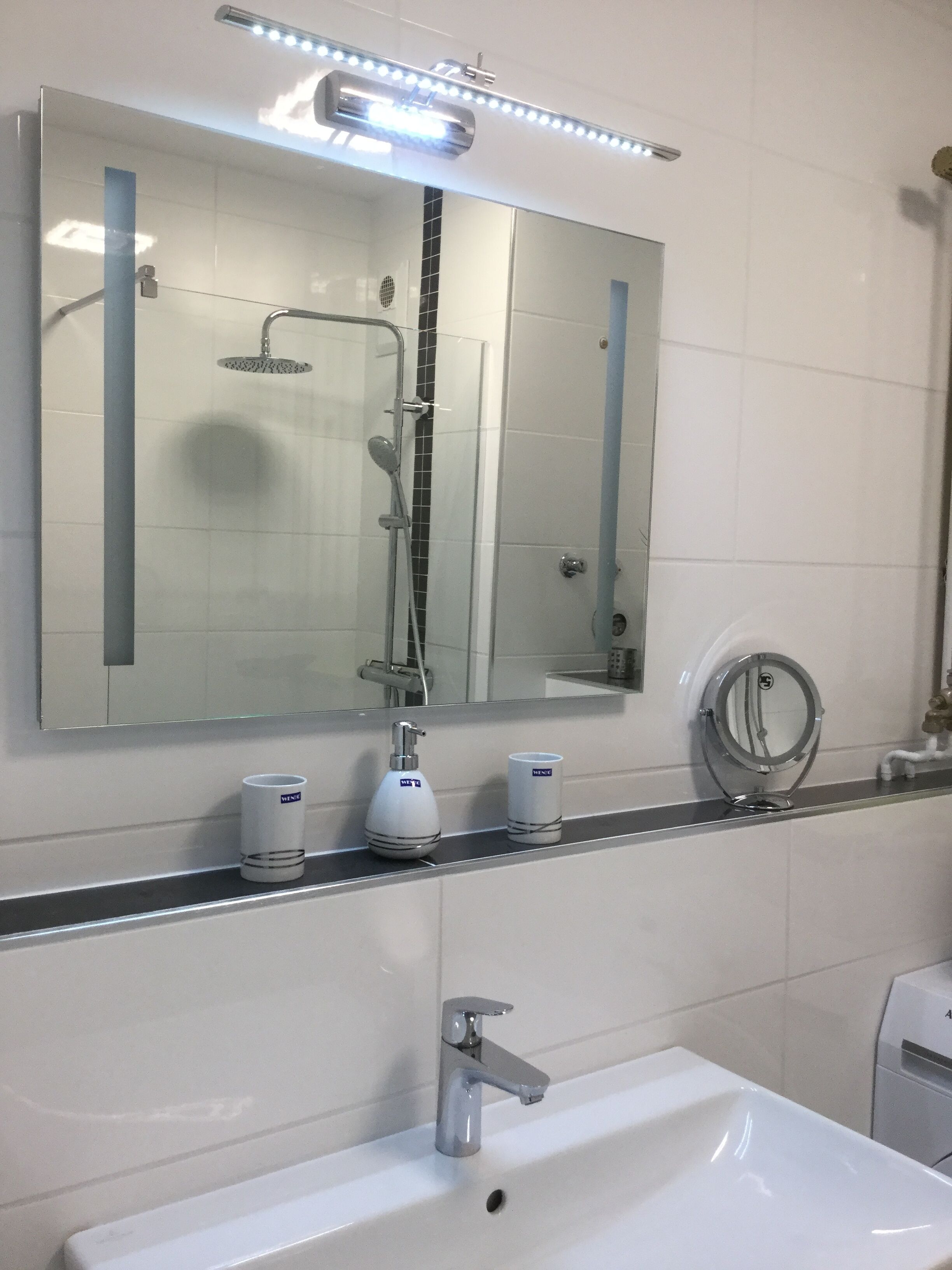 Un baño moderno con un espejo grande, una ducha, un lavabo y dos artículos de aseo.
