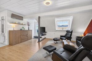 A modern living room with a TV, leather chairs, a sofa, and a dining area with a wooden table and chairs.