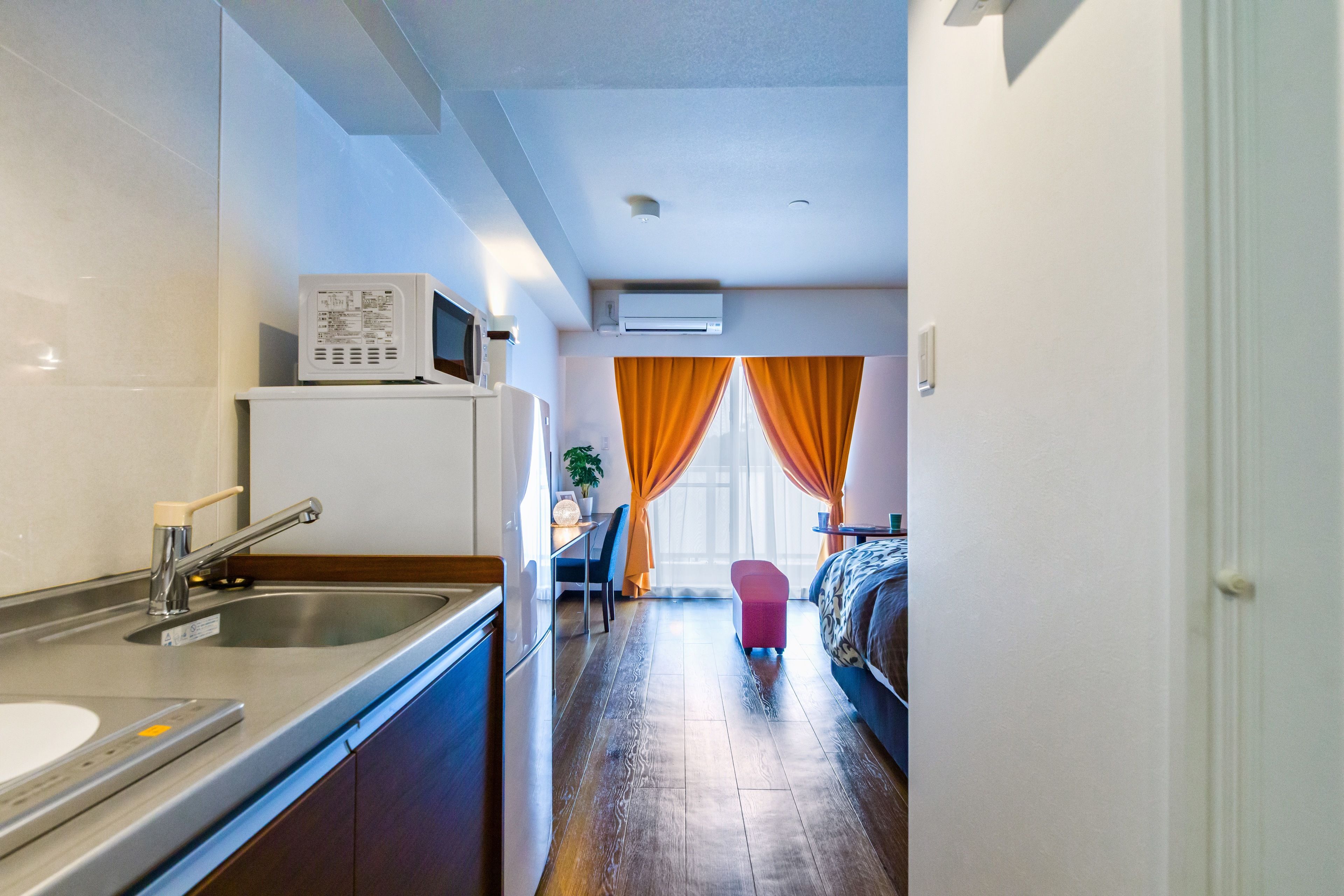 Et kompakt hotelværelse med tekøkken, seng, lille opholdsområde og et vindue med gardiner.