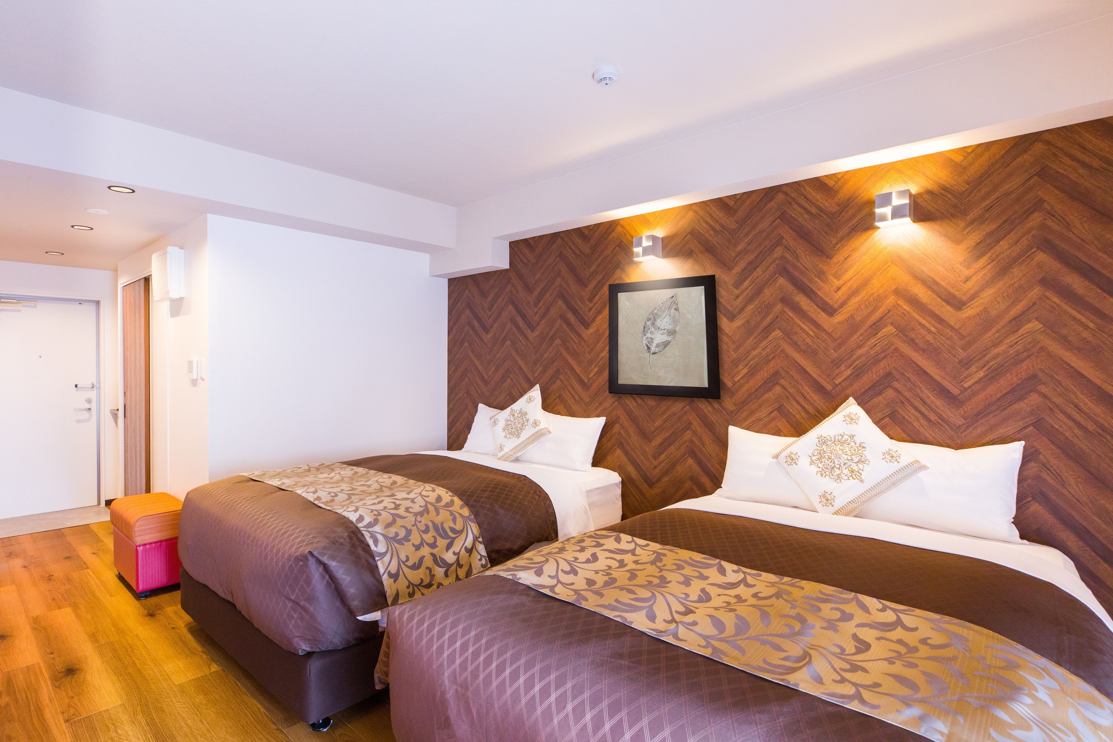 Ein Hotelzimmer mit zwei Betten, einer Wand mit Holzvertäfelung in Fischgrätmuster und einem gerahmten Kunstwerk darüber.