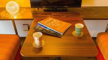Ein Hotelzimmer mit einem Holztisch, einem Buch mit dem Titel "Japan Brand Collection", zwei übereinander gestapelten Tassen und einem an der Wand montierten Fernseher.