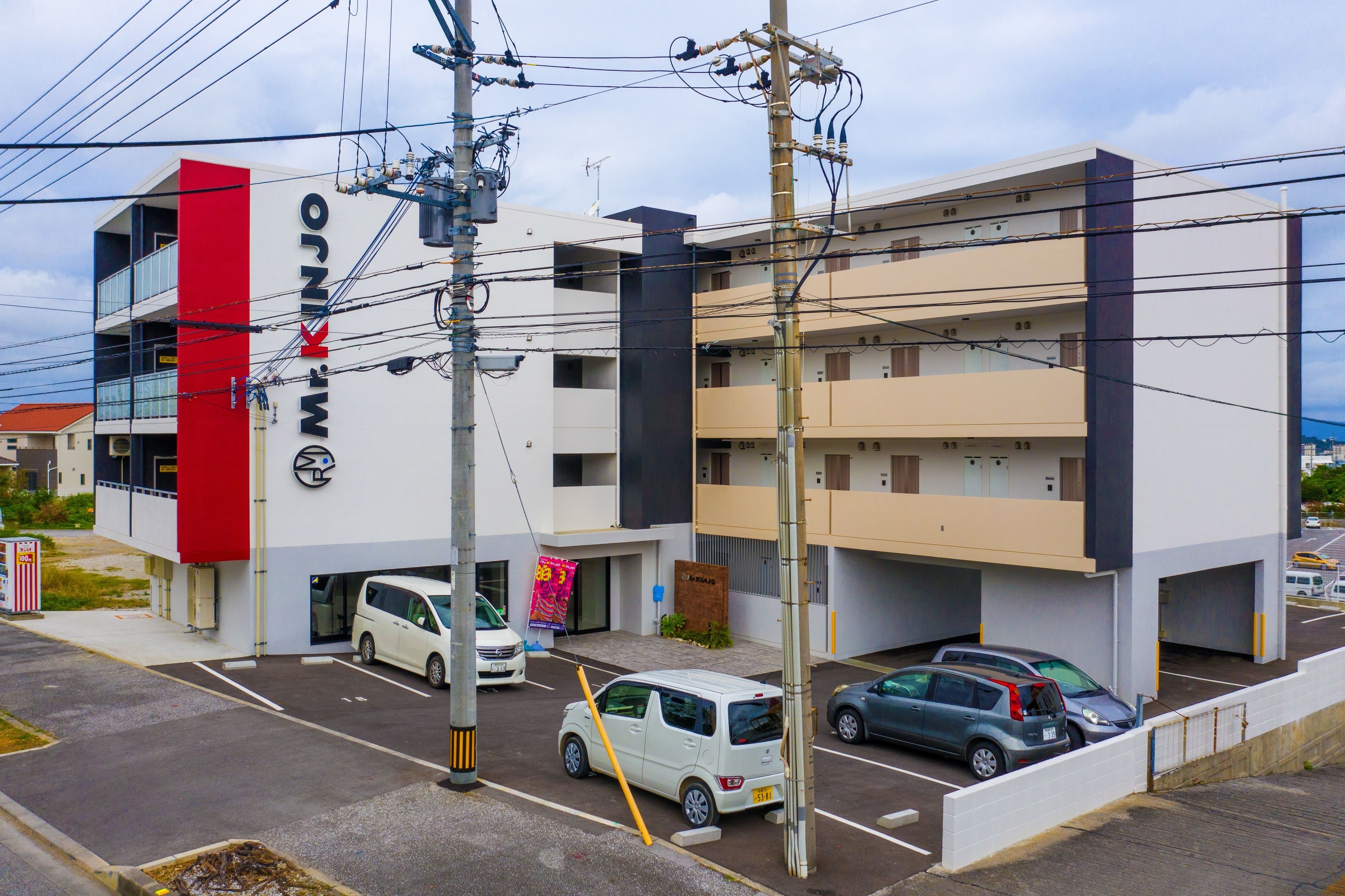 Un edificio de varios pisos con una franja vertical roja y un letrero que dice "Mr. KINJO".