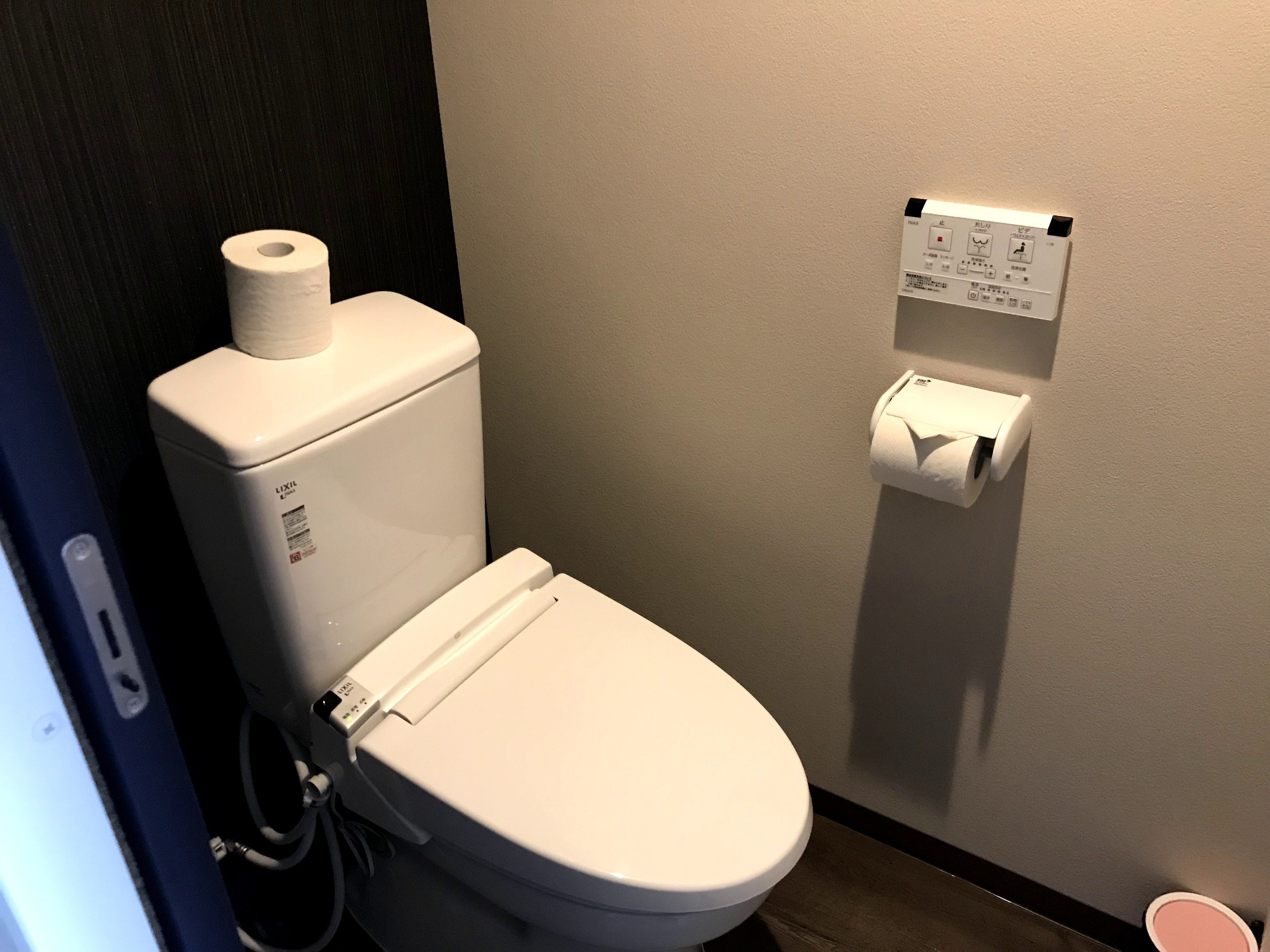 Un inodoro blanco con un dispensador de toallas de papel fijado en la pared a su lado.