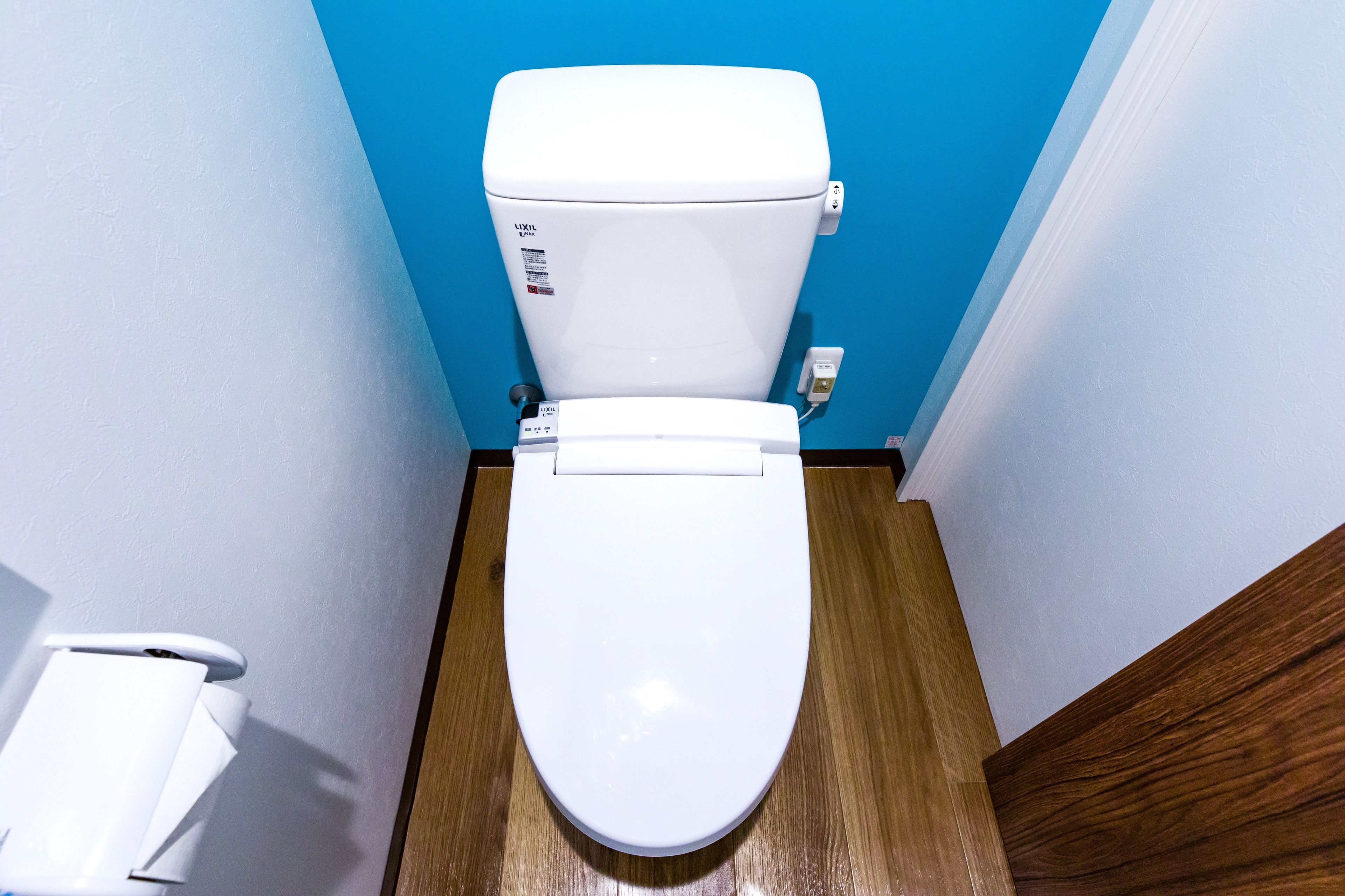 A white toilet with a blue wall and wooden floor in a bathroom.