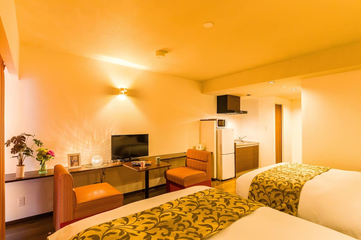 A hotel room with two beds, a desk with a computer, a chair, a refrigerator, and a television.