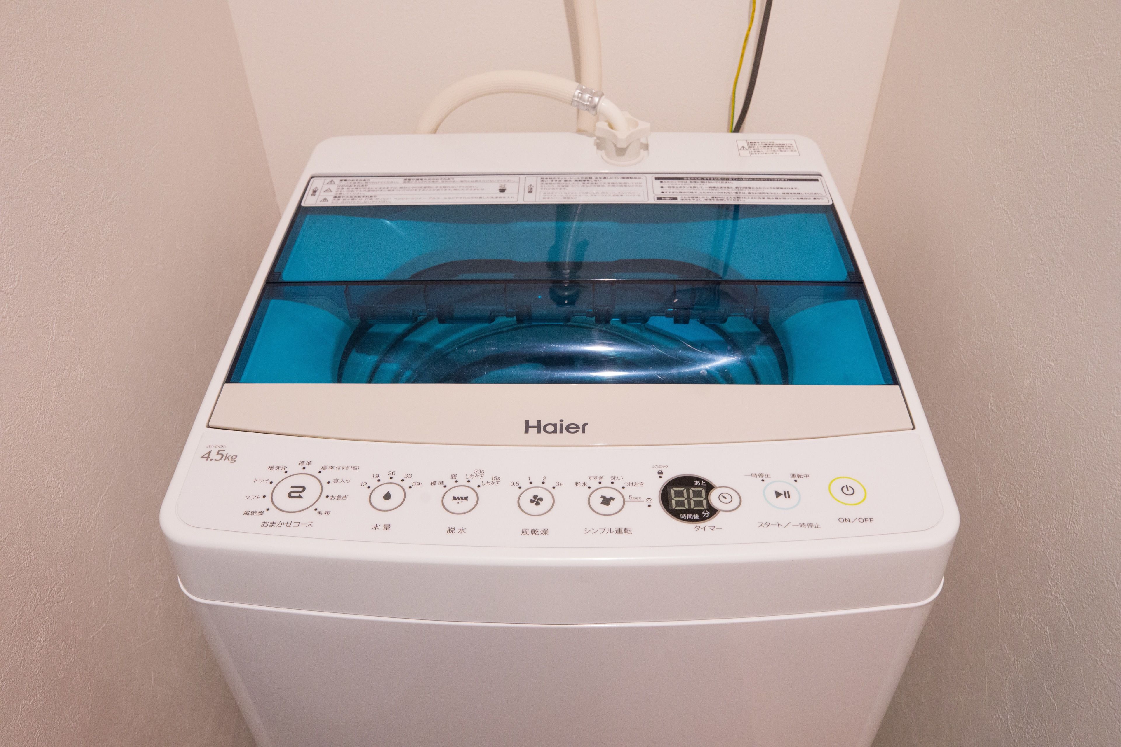 Una lavadora Haier blanca con un depósito de agua transparente, panel de control con diversas opciones y botón de encendido.