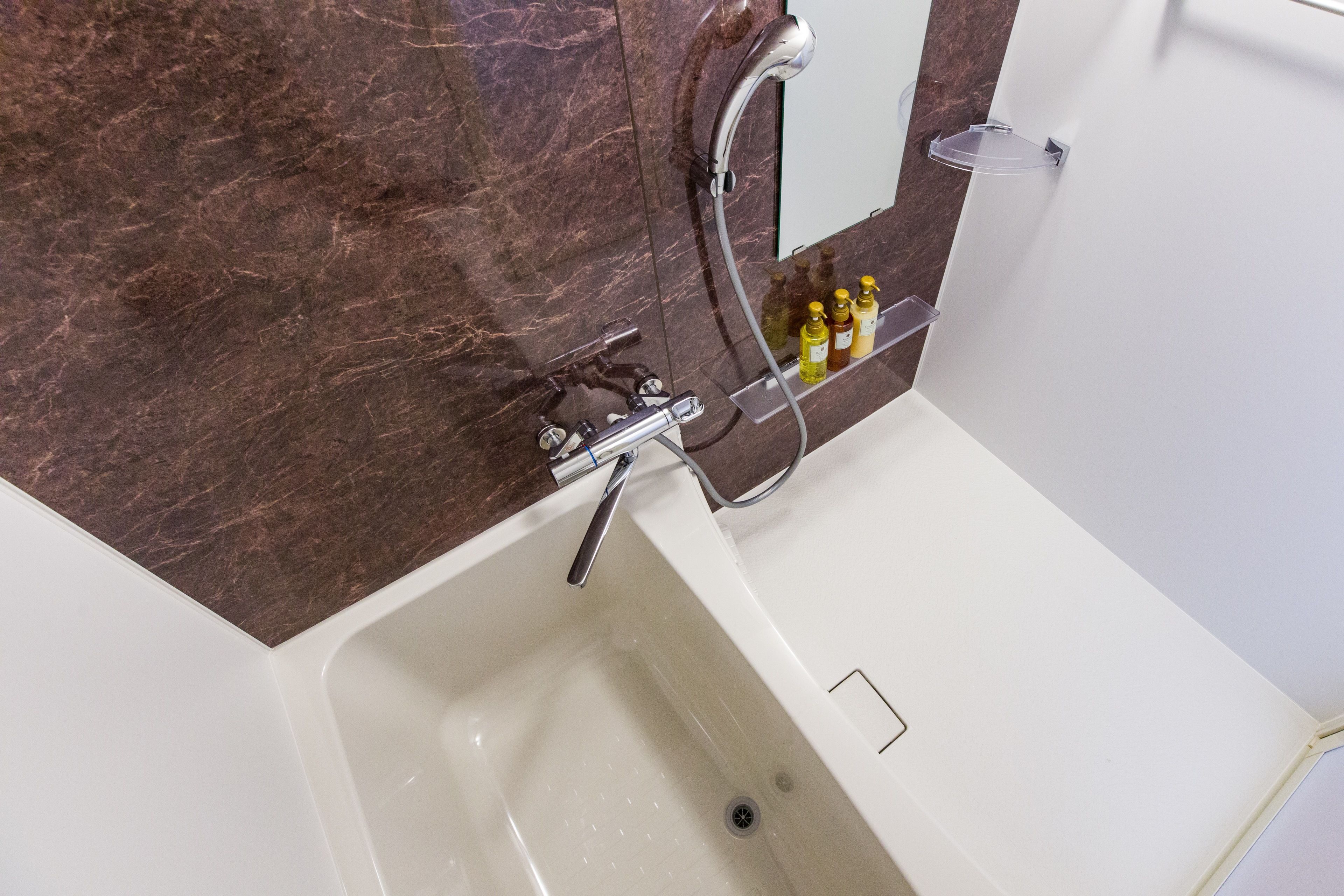A modern bathroom with a marble wall, a white bathtub, and a shower area.