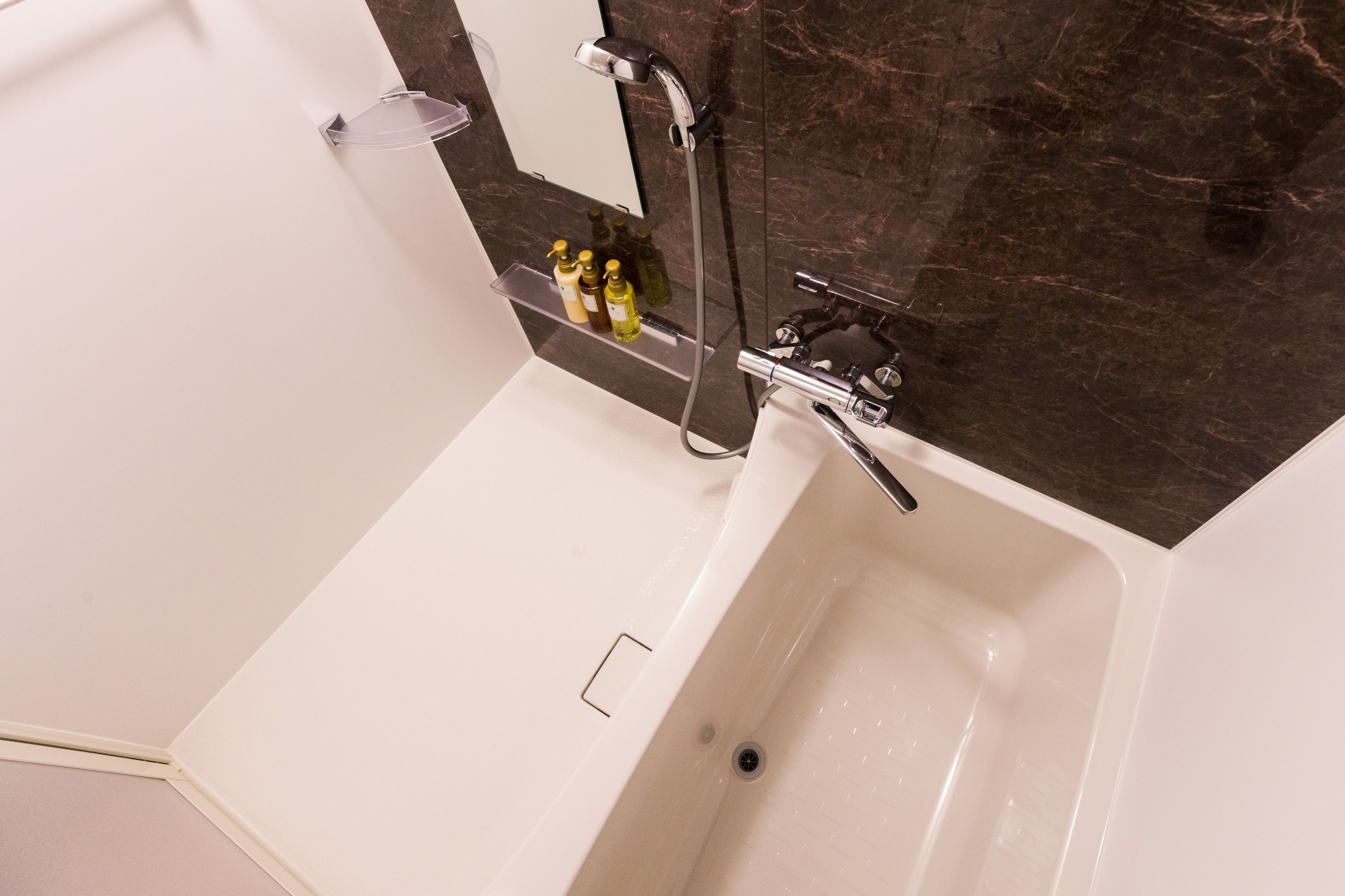 Une salle de bain moderne avec une baignoire blanche, une étagère en verre où sont rangés les articles de toilette et un mur en marbre.