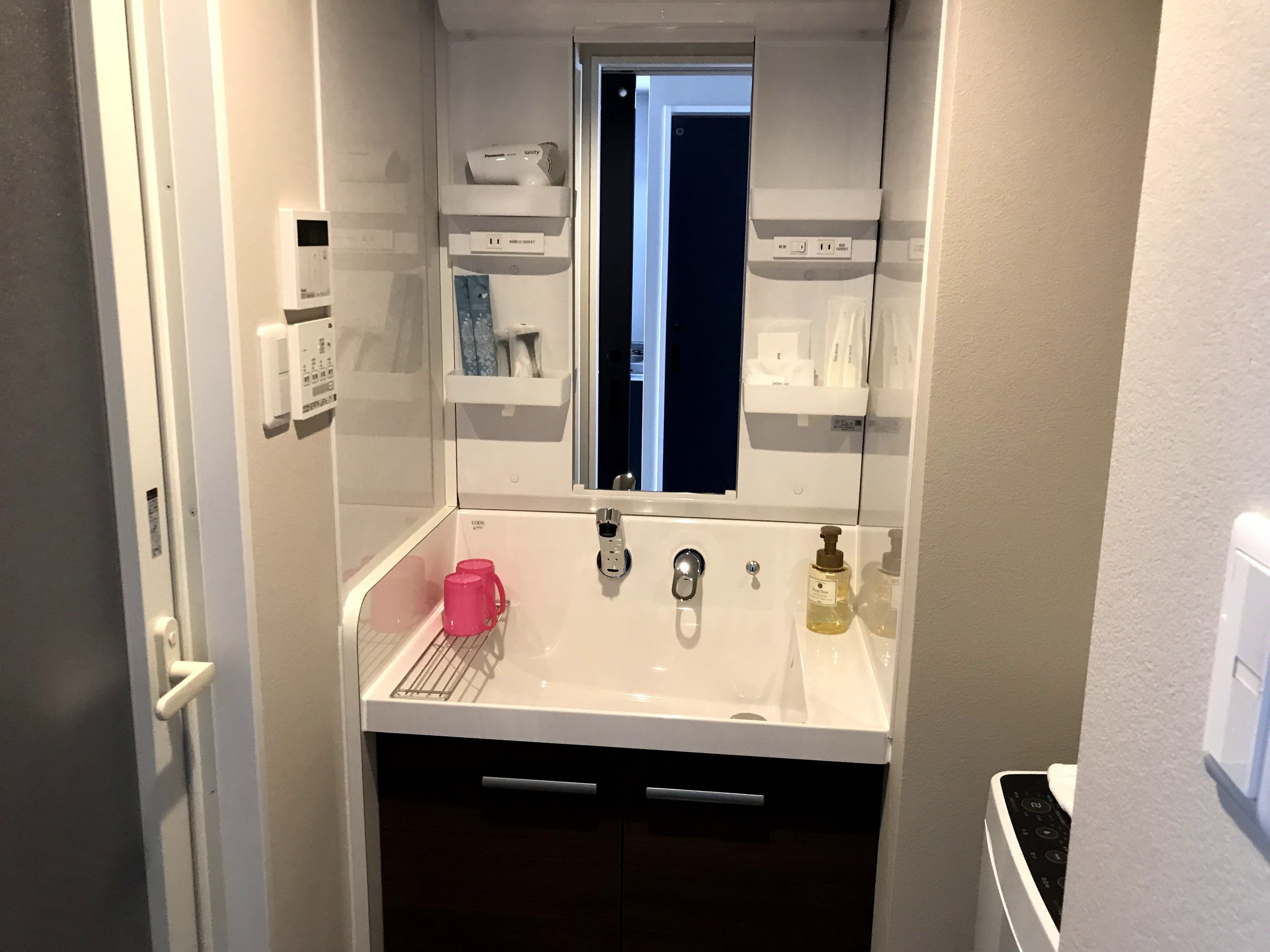 A compact bathroom with a white sink, a mirror, a window, and a door.