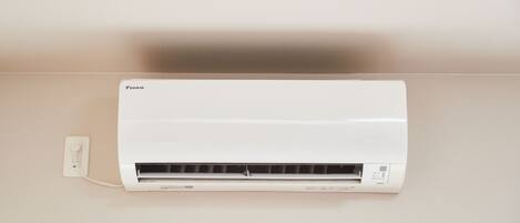 A white Daikin air conditioner mounted on a wall with a power outlet on the left.