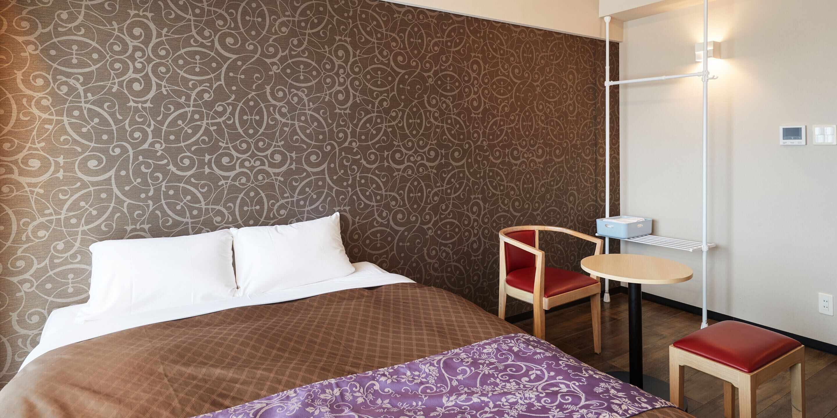 Una habitación de hotel con una cama grande, una mesita pequeña, una silla y una pared con un diseño decorativo.