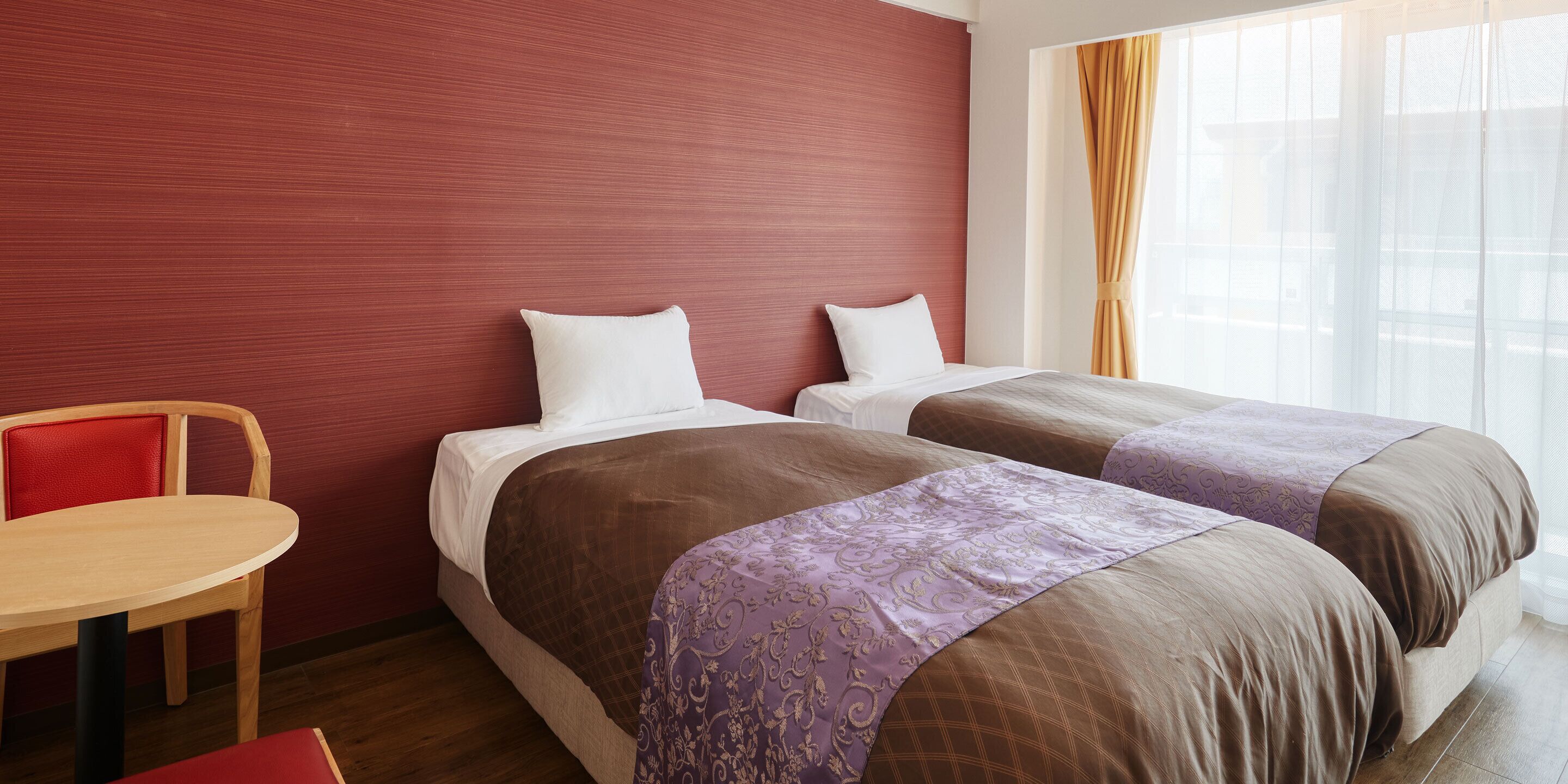 Une chambre d’hôtel avec deux lits, une table en bois et une chaise rouge.