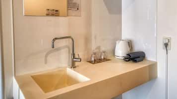 Un baño con lavamanos, espejo, toallero y cafetera.