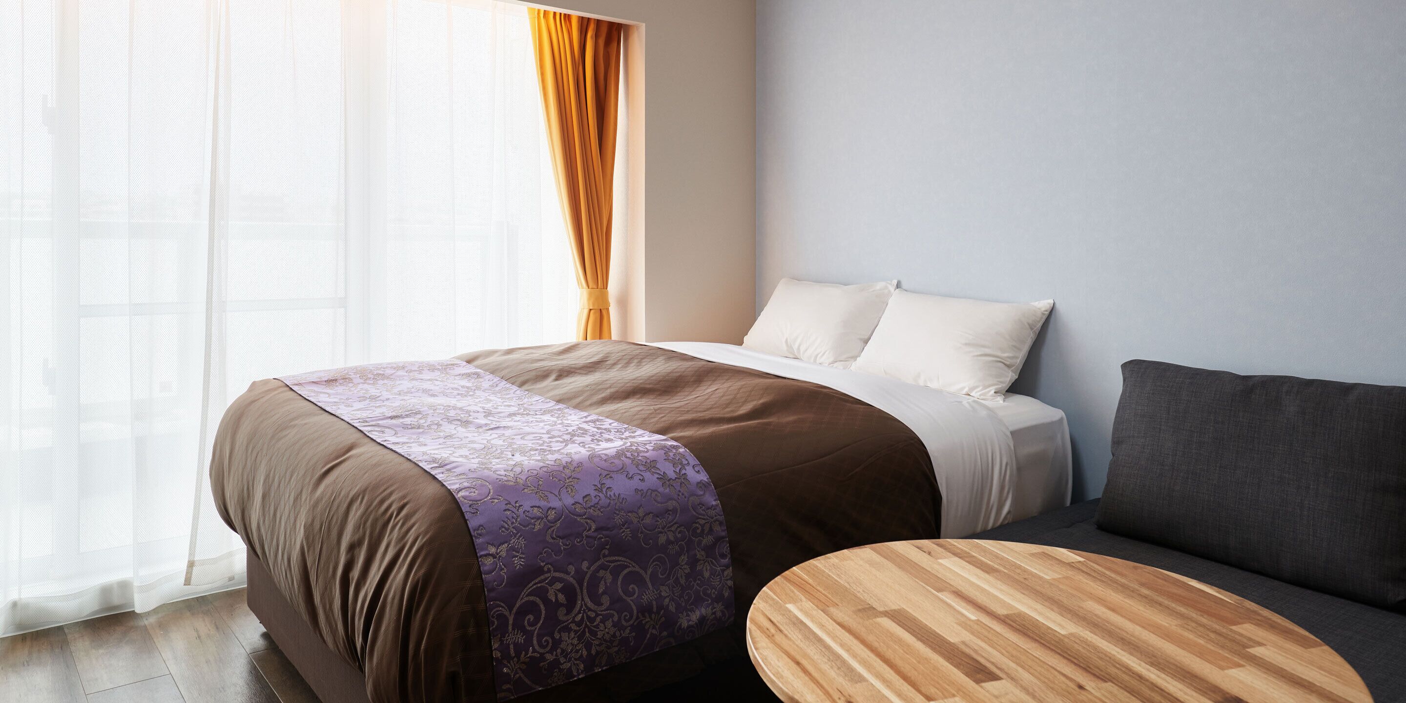 A modern hotel room with a large bed, a wooden side table, and a sofa.