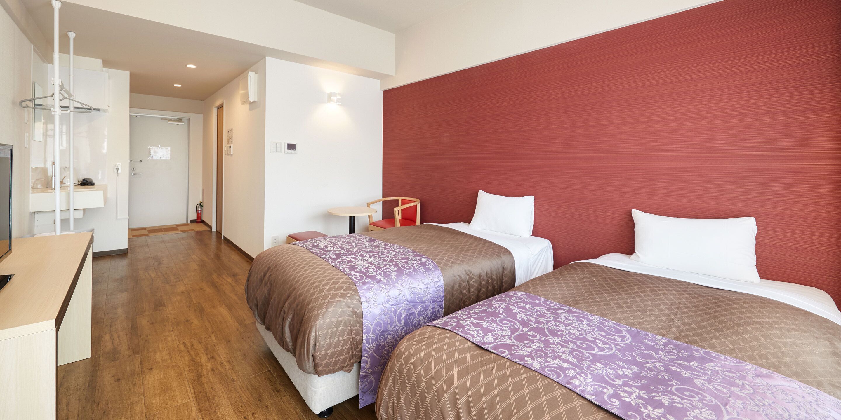 A hotel room with two beds, a desk, and a mirror.