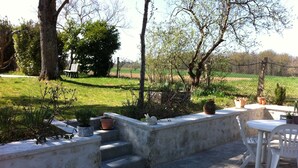 Un área de patio con mobiliario exterior, un banco de concreto y plantas en macetas.
