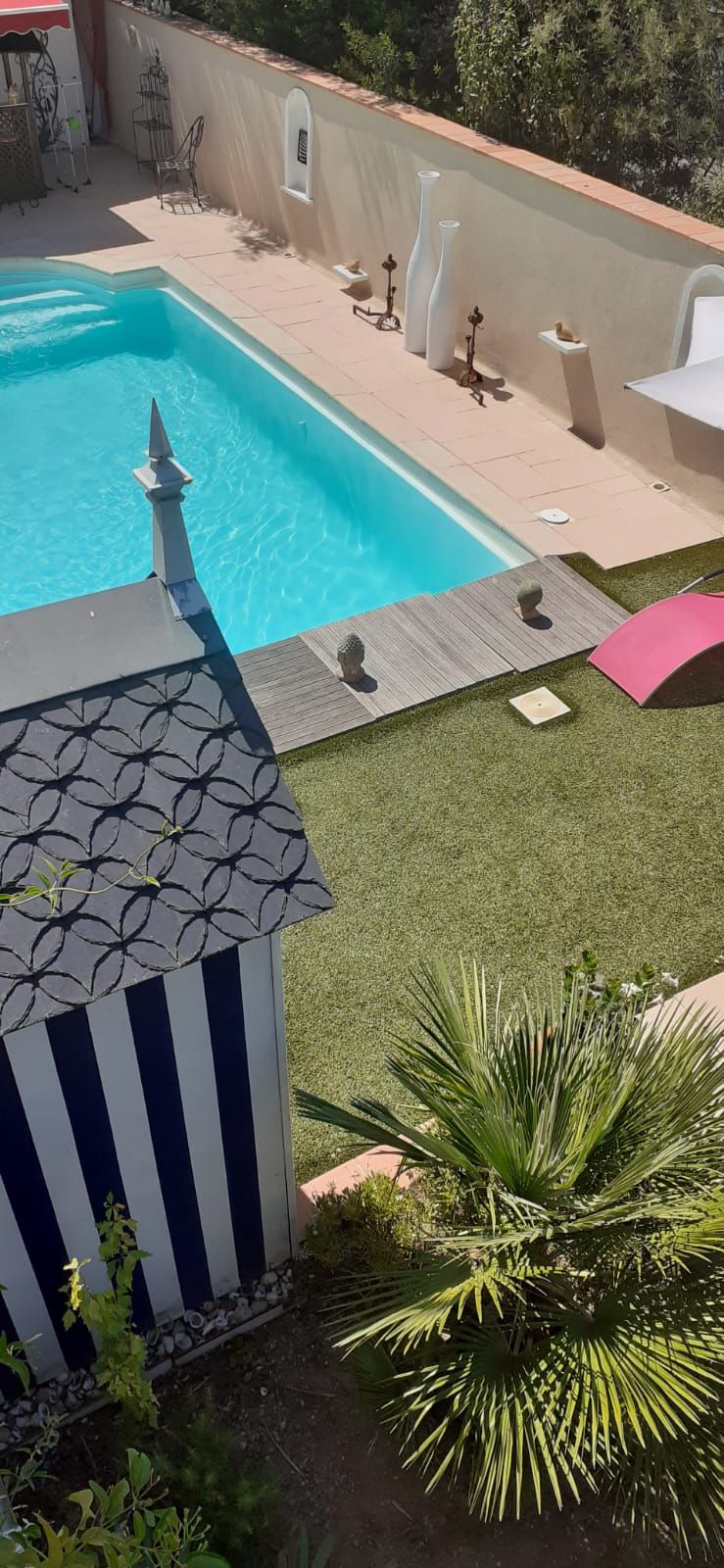 Ein Schwimmbecken mit Fliesen umgeben, umrahmt von einer niedrigen Mauer und einem kleinen Gartenbereich mit künstlichem Rasen und Pflanzen.
