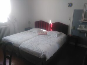 Un dormitorio con cama, una silla, mesita de noche, lámpara, radiador y baño con lavabo y espejo.