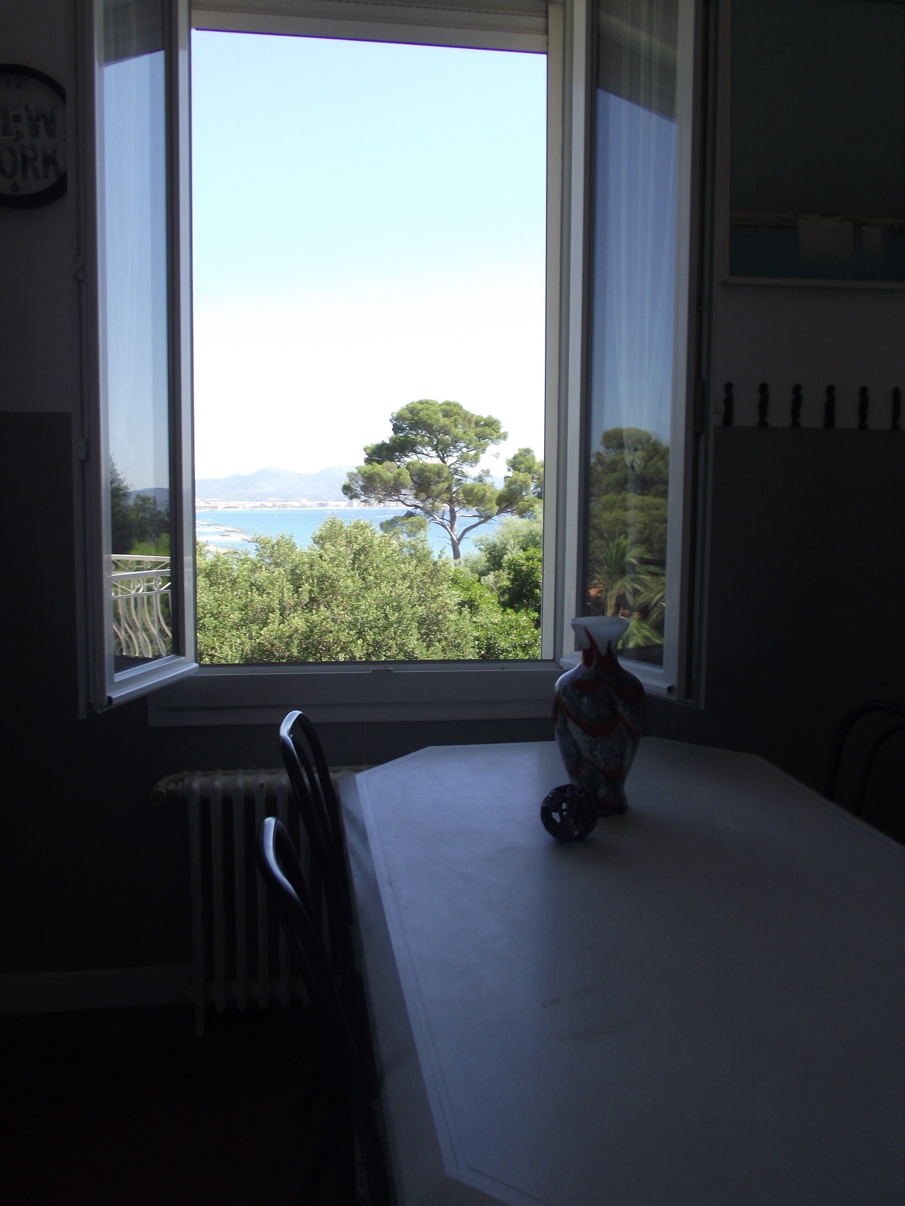 A dining area with a table and chairs, a vase on the table, and a view of trees and water through a window.
