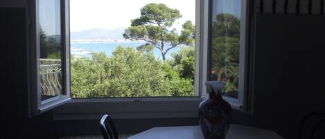 A dining area with a table and chairs, a vase on the table, and a view of trees and water through a window.