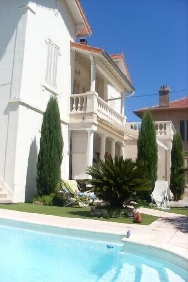 Un edificio blanco con balcón, piscina y vegetación.