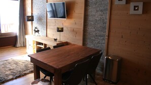 Una mesa de comedor de madera con sillas, un televisor montado en la pared y cuadros enmarcados.