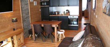 A cozy interior with a wooden dining area, a sofa, and a kitchen with dark cabinets and a tiled backsplash.