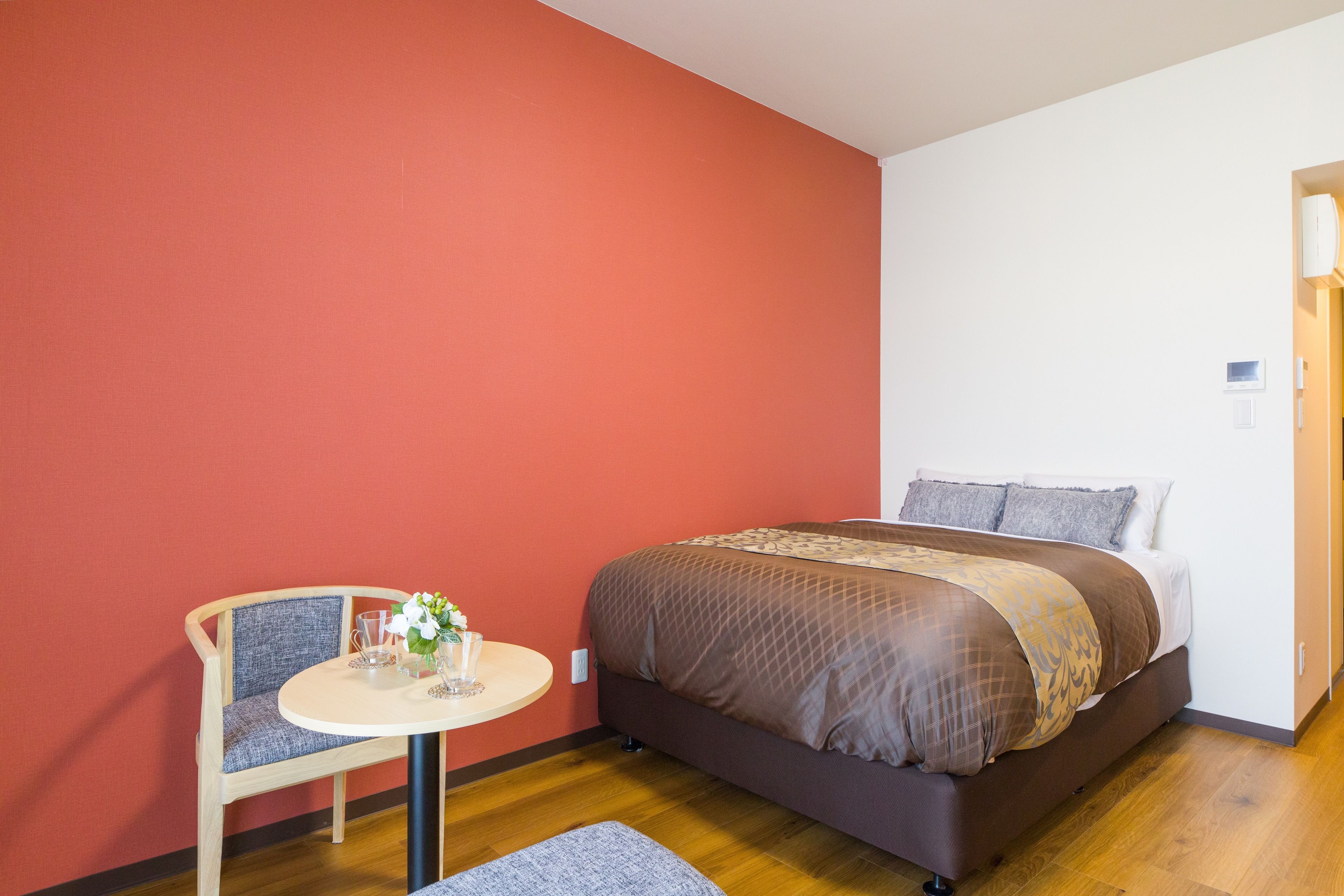A bedroom with a bed, a chair, a small table, and a red wall.