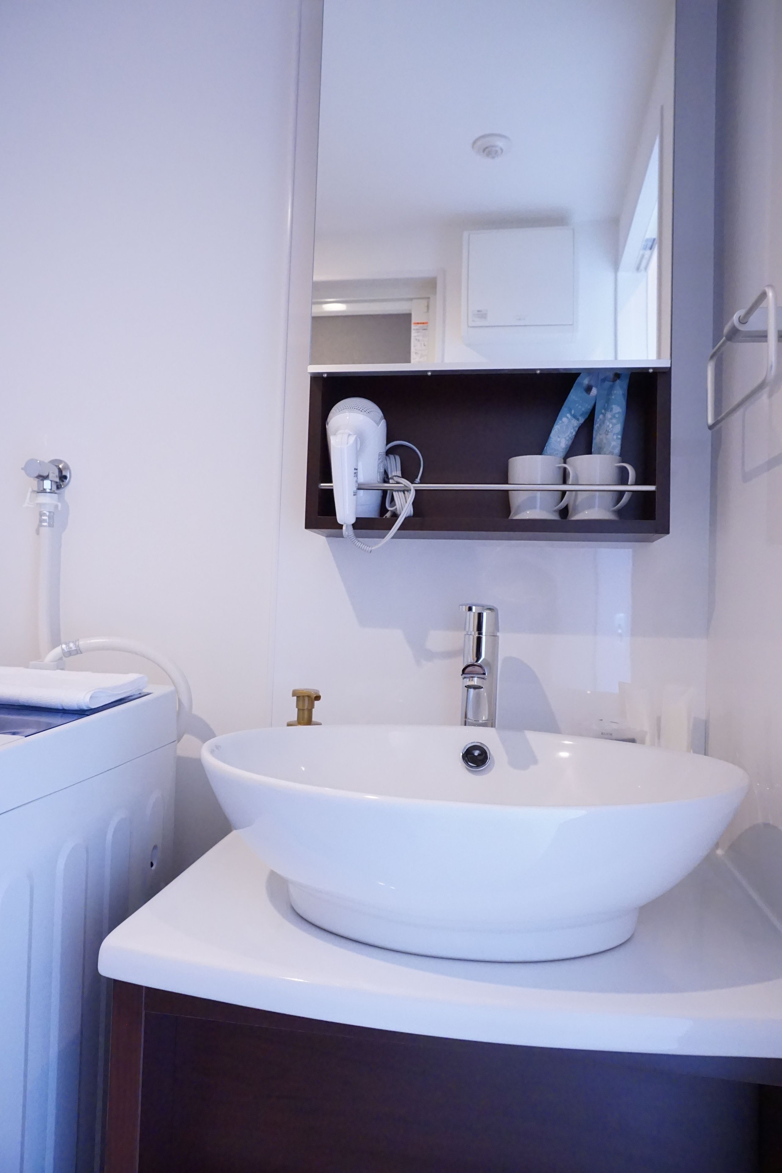Un baño moderno con un lavamanos blanco, un espejo encima y un secador de pelo en un estante.