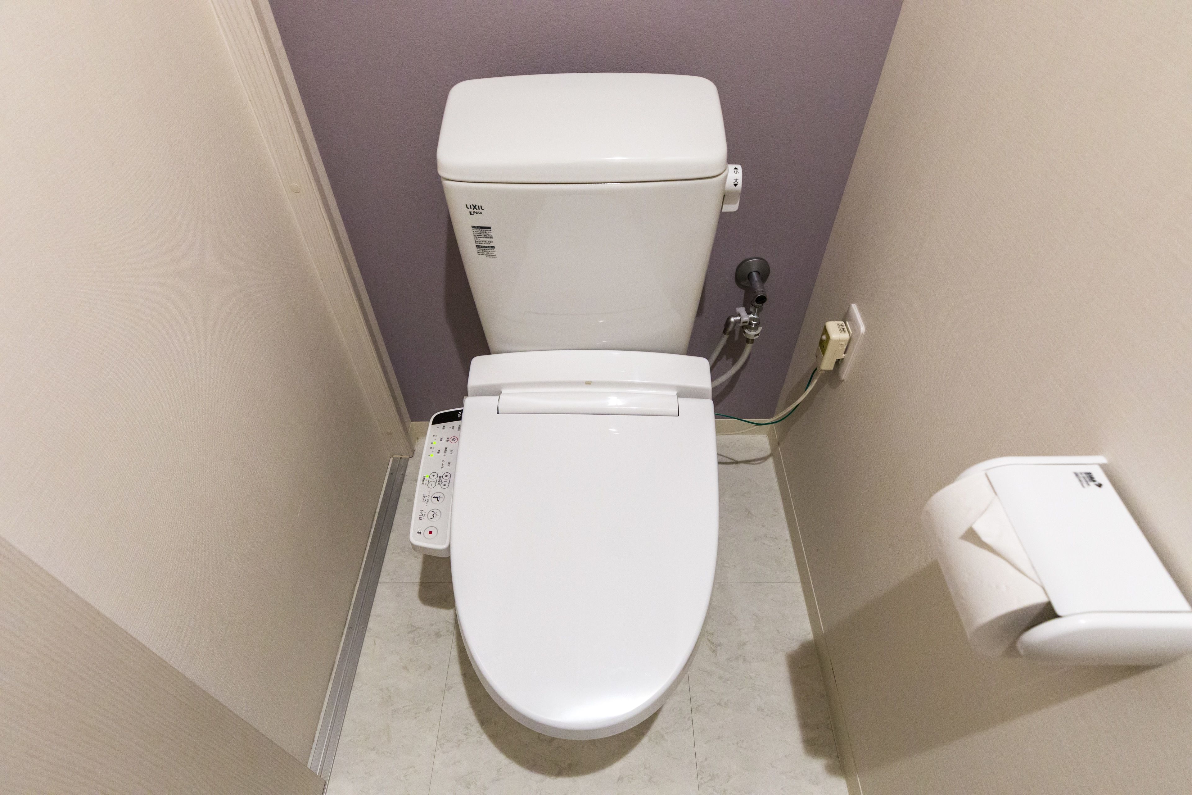 A white toilet with a control panel, a toilet paper holder, and a wall-mounted flush button.