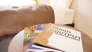 A round wooden table with a stack of magazines and a book titled "High Output Management" on it.