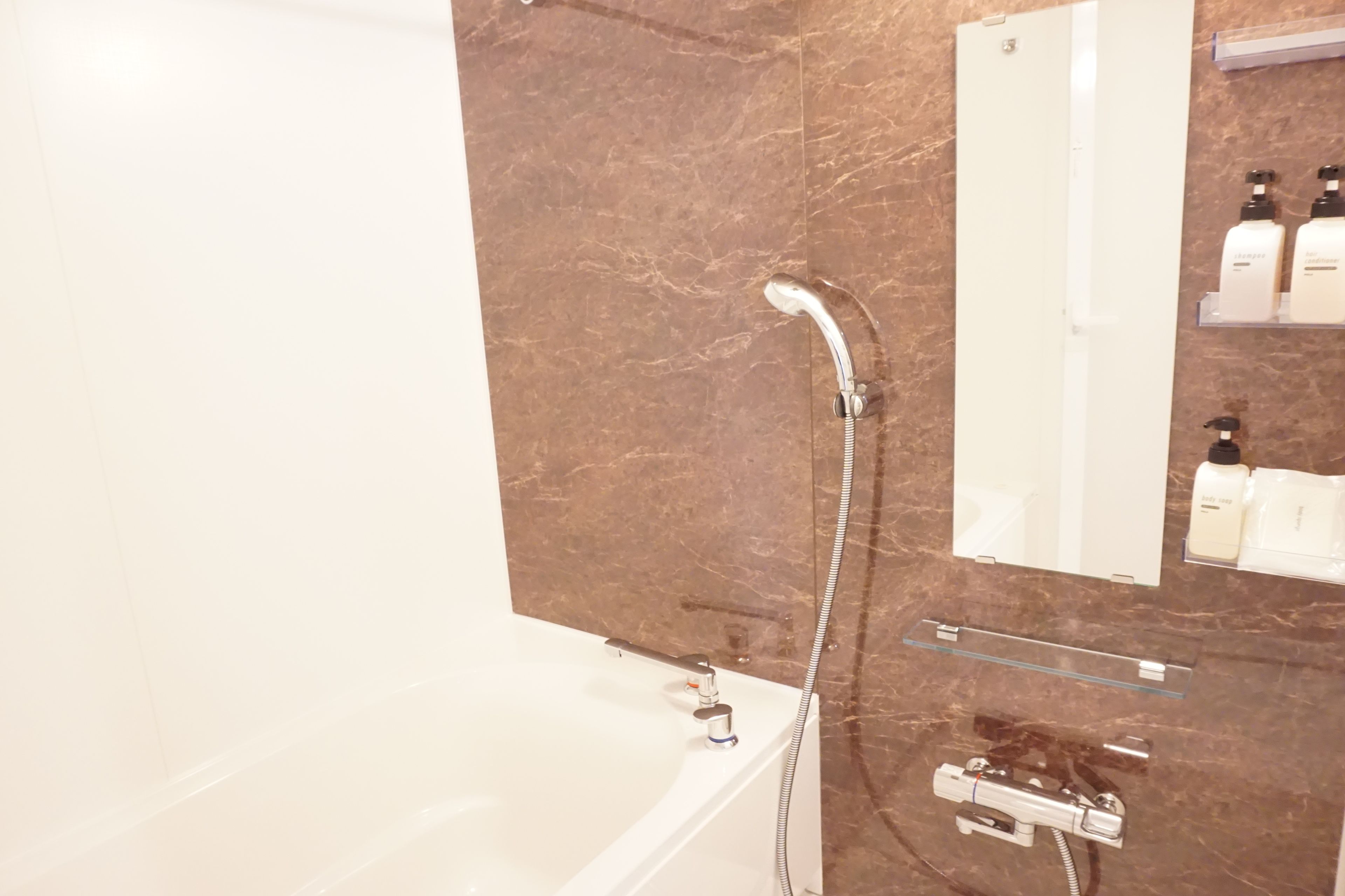 A modern bathroom with a marble wall, a bathtub, a shower, and a mirror.