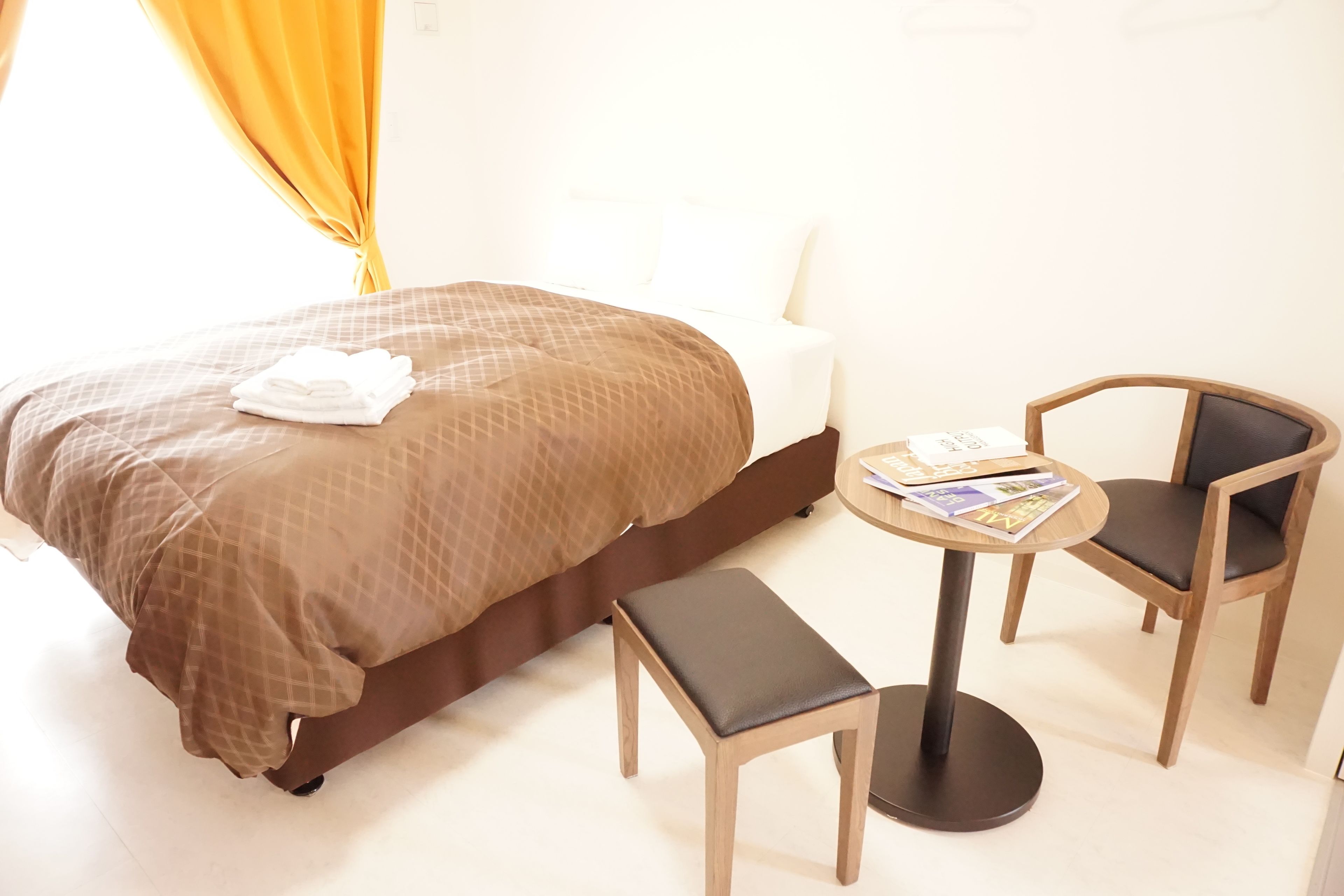 A hotel room with a bed, a small table with magazines, two chairs, and a bench.