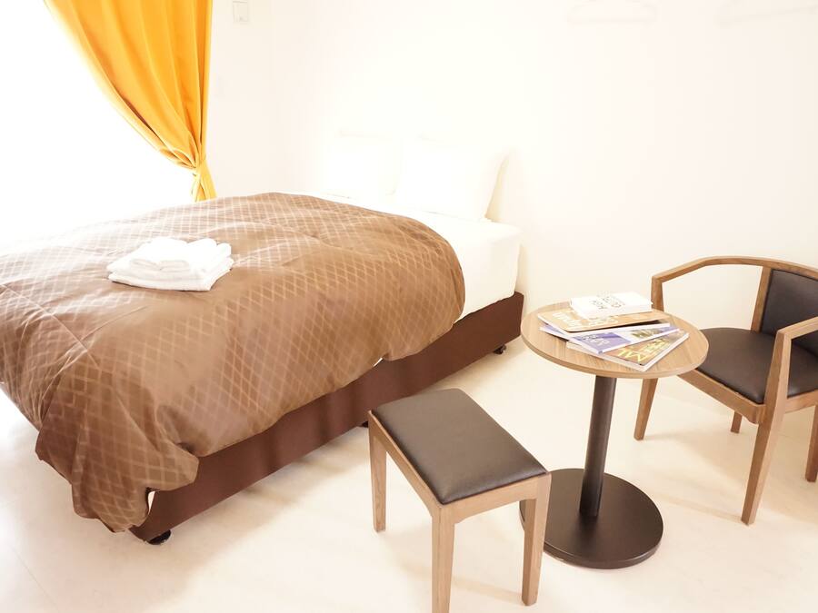 A hotel room with a bed, a small table with magazines, two chairs, and a bench.
