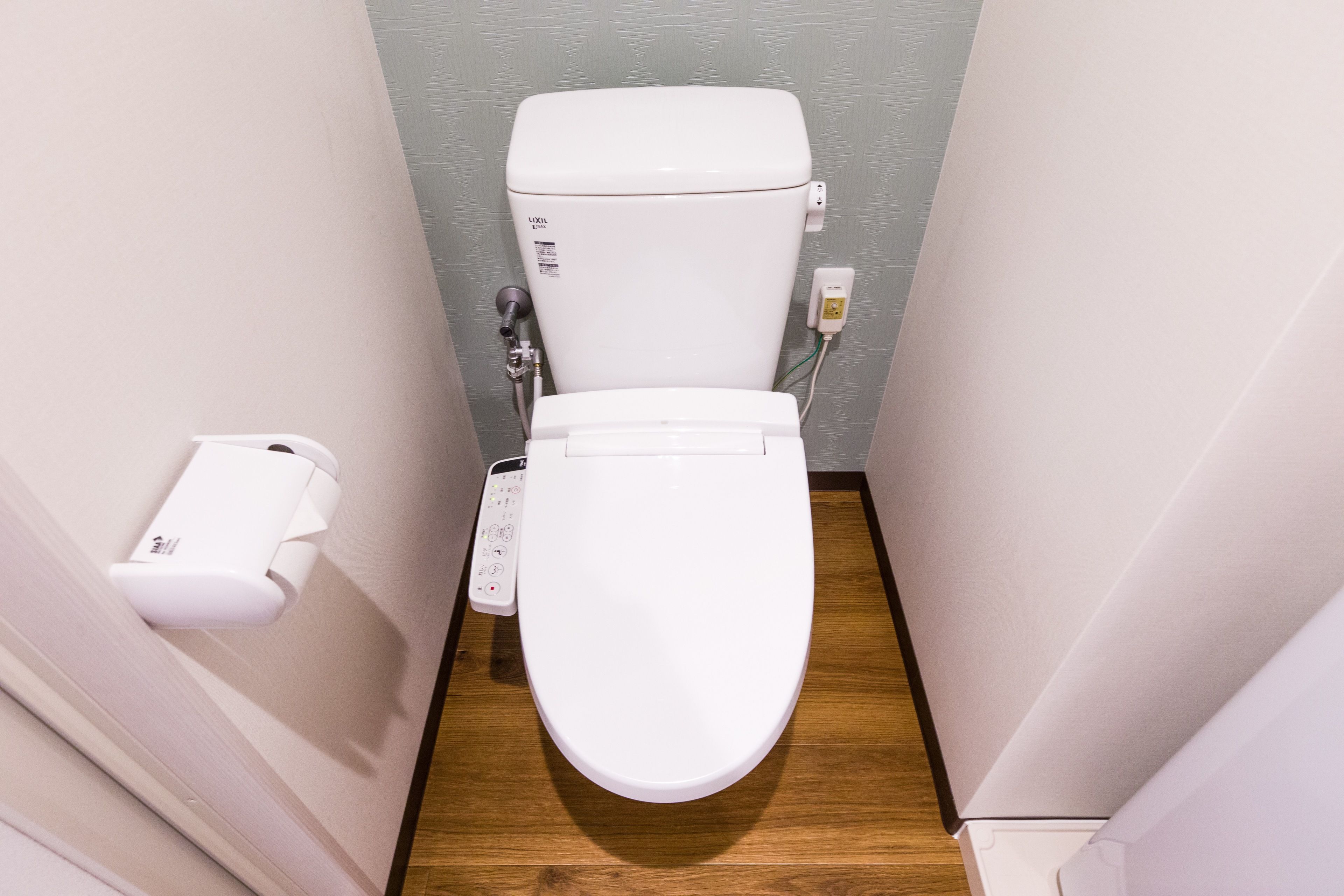 A compact, modern bathroom with a white toilet, a wall-mounted bidet, and a control panel.