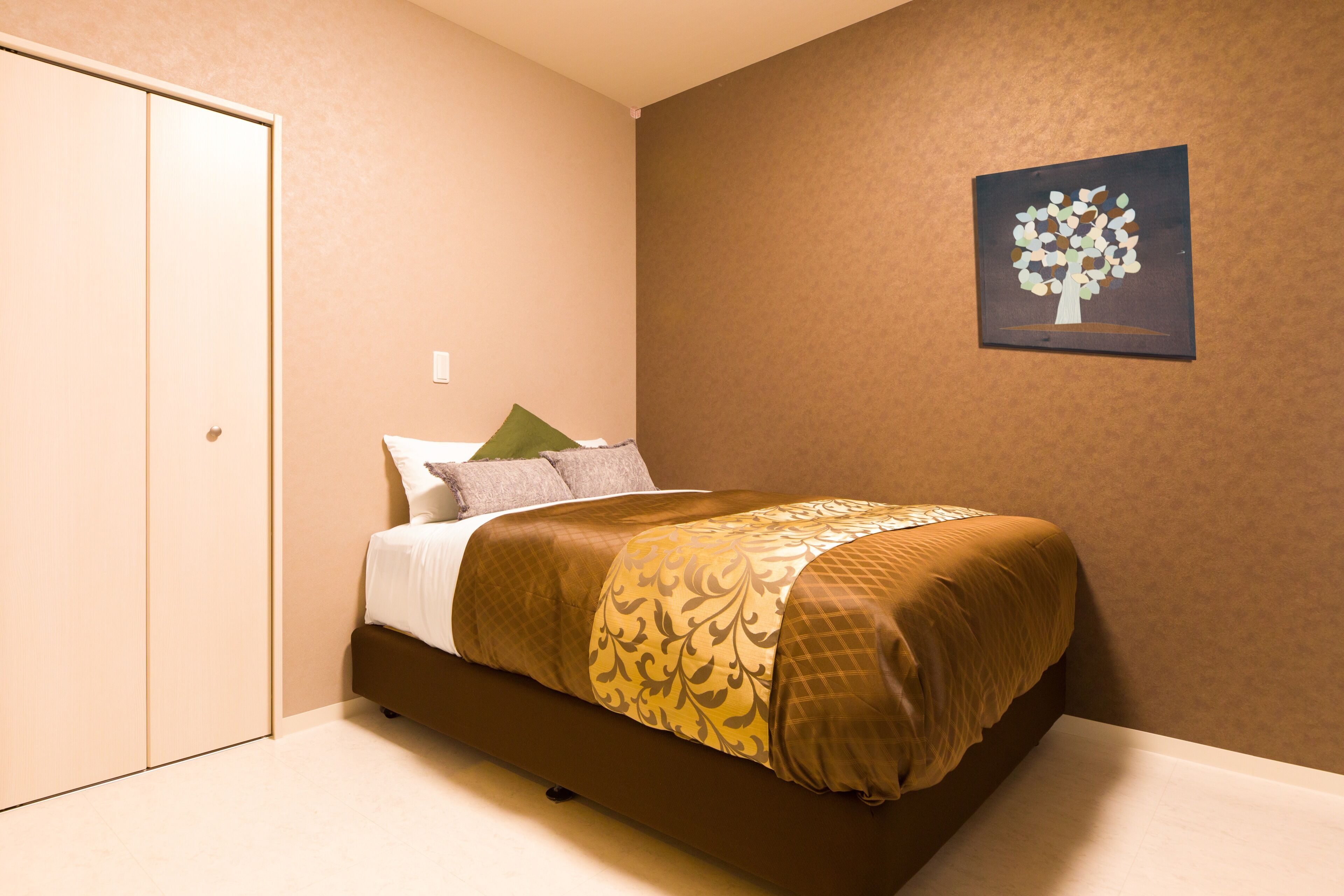 A bedroom with a bed, pillows, a blanket, a wall-mounted painting, and a door.