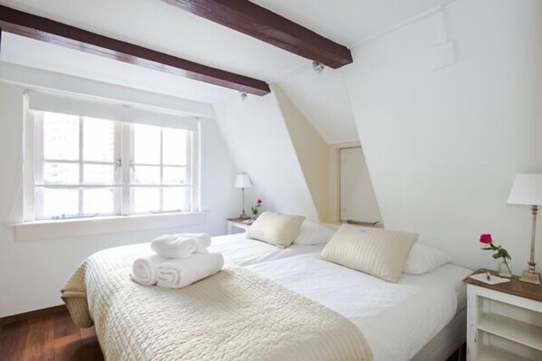 A bedroom with a large bed, a window, and a nightstand with a lamp.