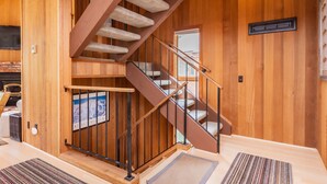 Un intérieur en bois avec un escalier, une cheminée et une vue sur l’extérieur.