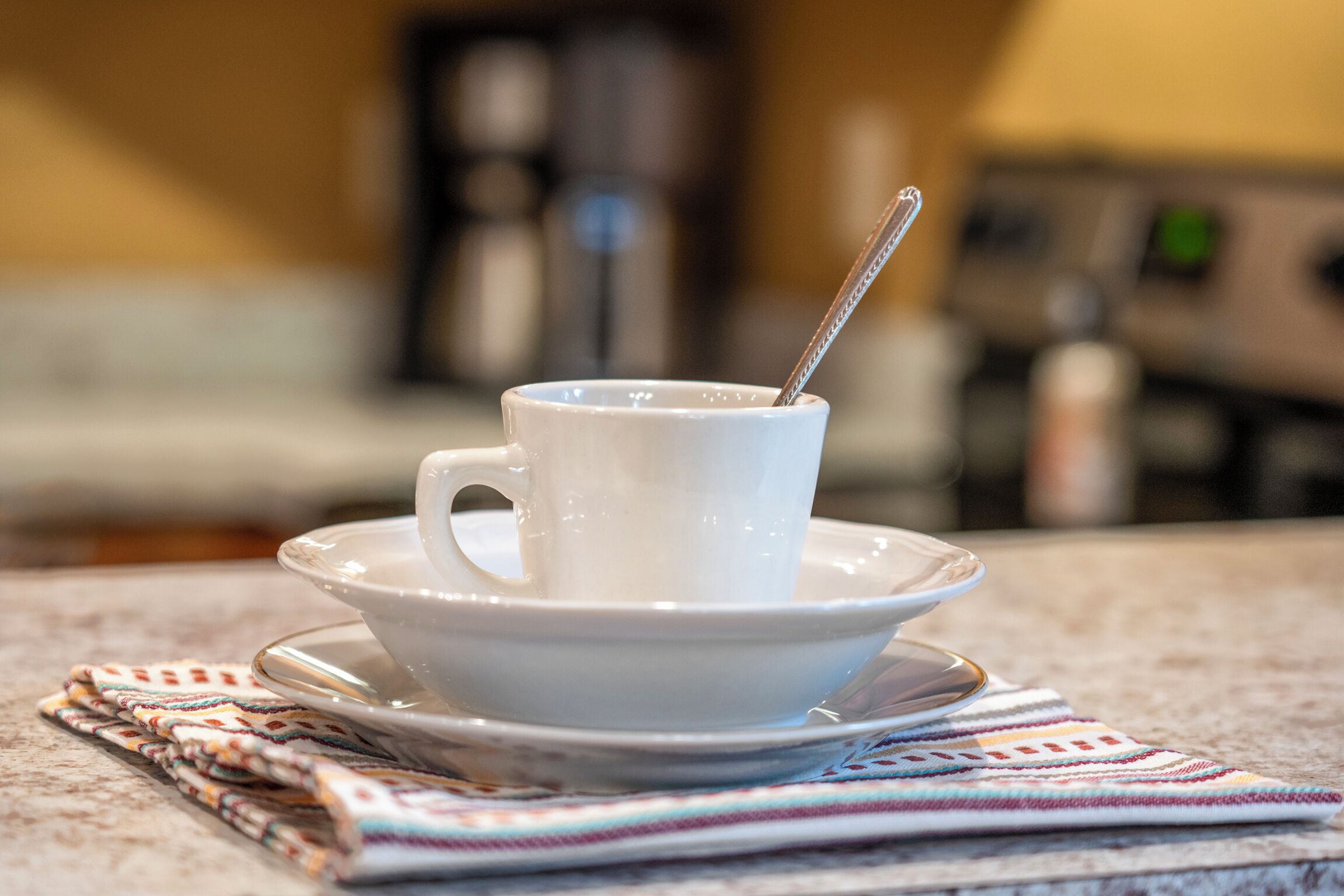 Eine weiße Tasse und Untertasse auf einer Marmorarbeitsplatte mit einem gestreiften Servietttuch darunter.