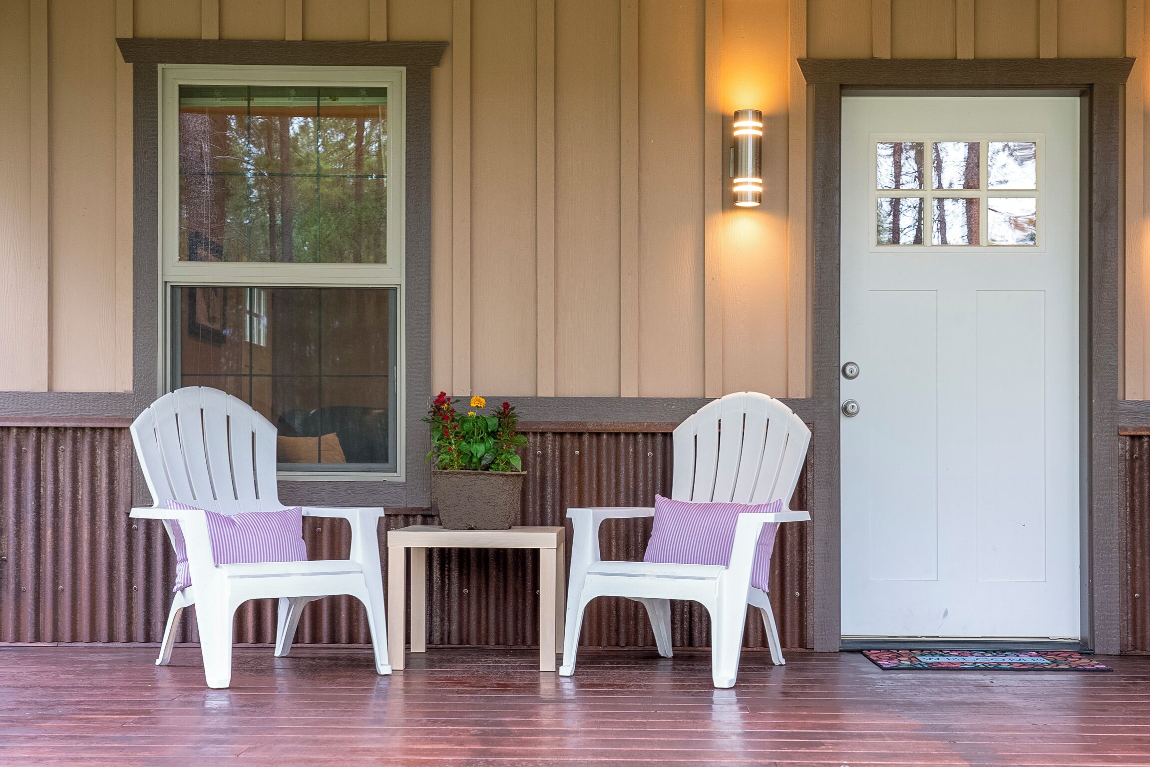 A porch with two white Adirondack chairs, a small table, and a potted plant.