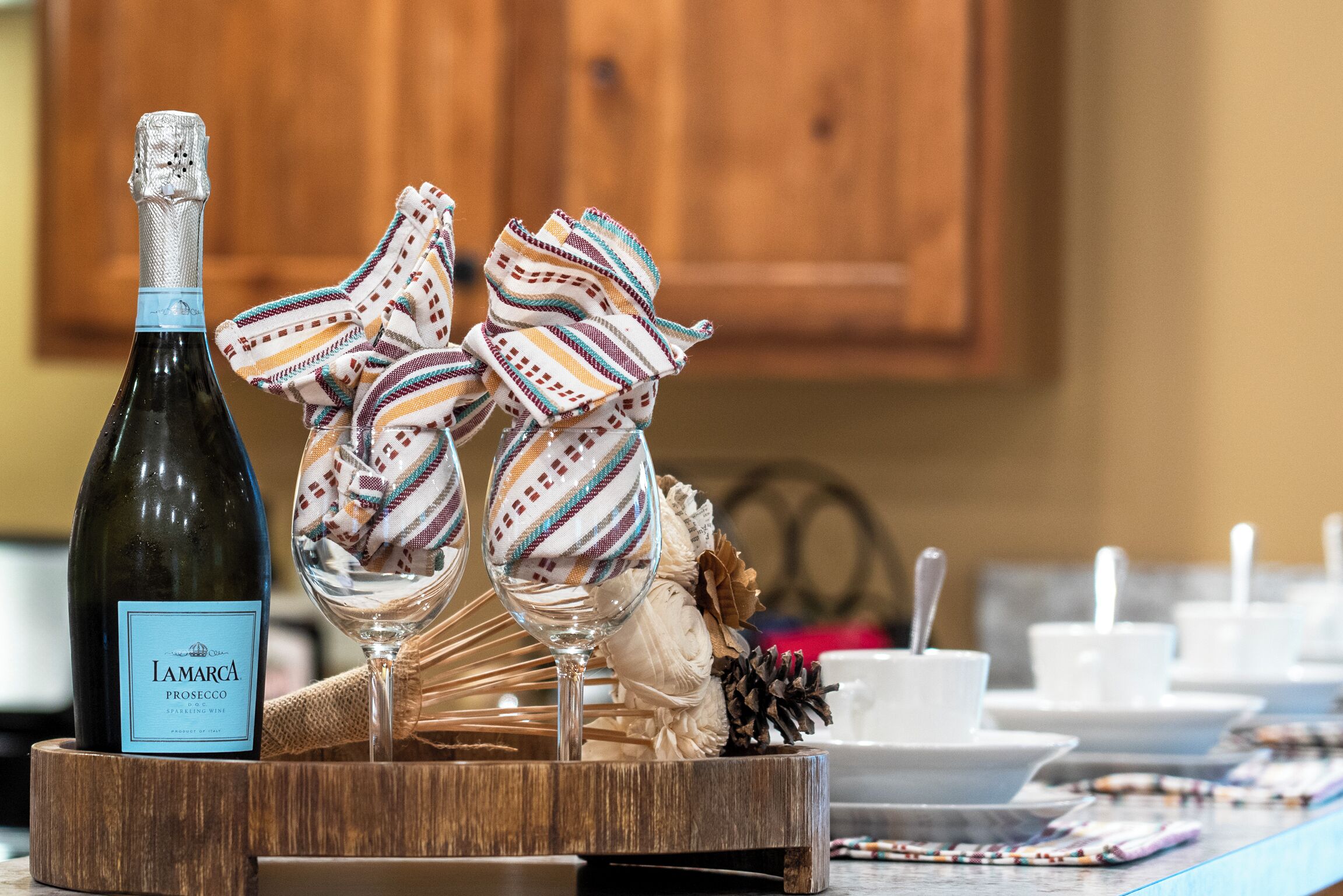 A bottle of Iamarca Prosecco on a wooden tray with two glasses and decorative napkins.