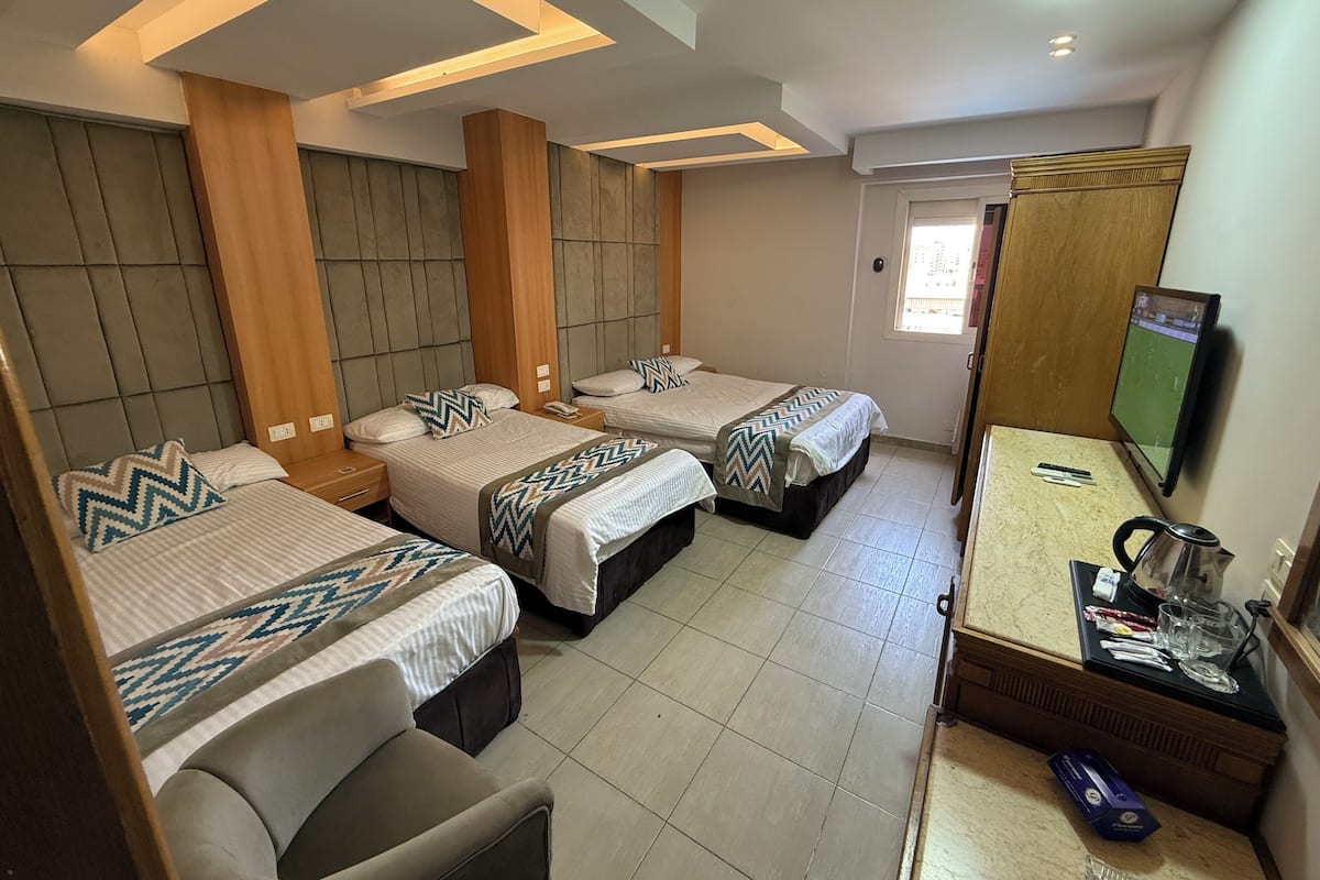 A hotel room with three beds, a TV, a coffee maker, and a small table with glasses and a kettle.